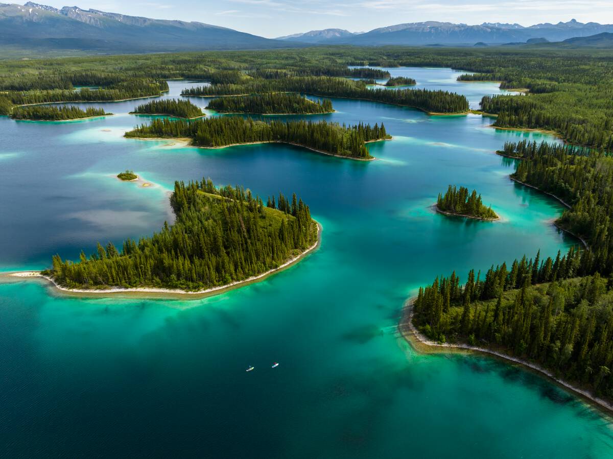aerial landscape of vibrant aquamarine waters and paddlers in Tā Ch'ilā Provincial Park (Boya Lake)